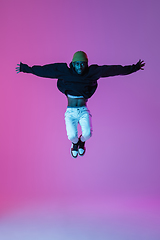 Image showing Young stylish man in modern street style outfit isolated on gradient background in neon light. African-american fashionable model in look book, musician performing.