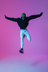 Image showing Young stylish man in modern street style outfit isolated on gradient background in neon light. African-american fashionable model in look book, musician performing.