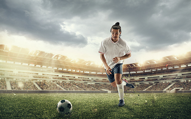 Image showing Male soccer, football player catching ball in jump at the stadium during sport match on dark sky background