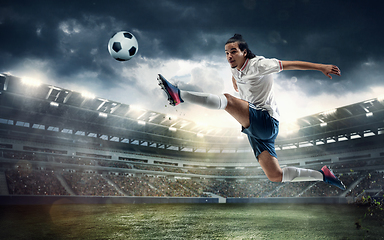 Image showing Male soccer, football player catching ball in jump at the stadium during sport match on dark sky background