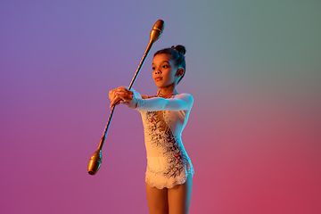 Image showing African-american rhythmic gymnast, pretty girl practicing on gradient studio background in neon light