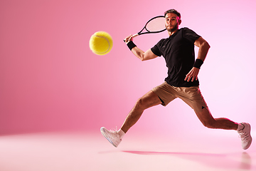 Image showing Young caucasian man playing tennis isolated on pink studio background, action and motion concept