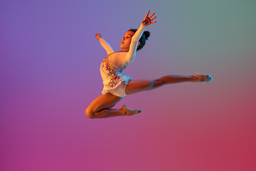 Image showing African-american rhythmic gymnast, pretty girl practicing on gradient studio background in neon light