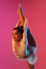 Image showing African-american rhythmic gymnast, pretty girl practicing on gradient studio background in neon light