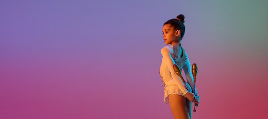 Image showing African-american rhythmic gymnast, pretty girl practicing on gradient studio background in neon light