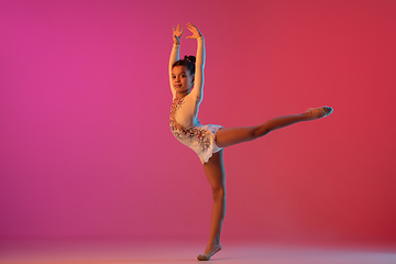 Image showing African-american rhythmic gymnast, pretty girl practicing on gradient studio background in neon light