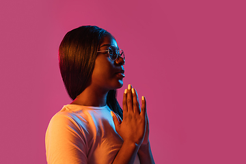 Image showing African young woman\'s portrait on pink studio background in neon. Concept of human emotions, facial expression, youth, sales, ad.