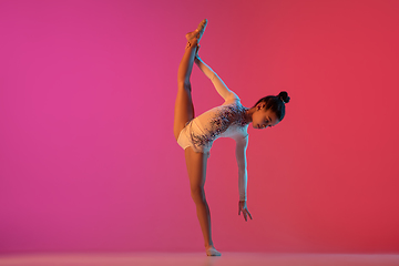 Image showing African-american rhythmic gymnast, pretty girl practicing on gradient studio background in neon light