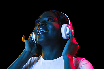 Image showing African young woman\'s portrait on dark studio background in neon. Concept of human emotions, facial expression, youth, sales, ad.