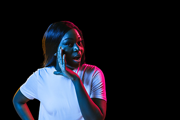 Image showing African young woman\'s portrait on dark studio background in neon. Concept of human emotions, facial expression, youth, sales, ad.