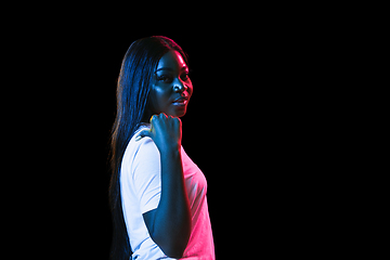 Image showing African young woman\'s portrait on dark studio background in neon. Concept of human emotions, facial expression, youth, sales, ad.