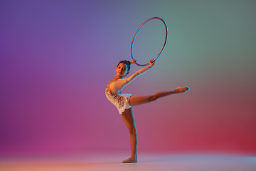 Image showing African-american rhythmic gymnast, pretty girl practicing on gradient studio background in neon light