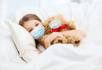 Image showing girl wearing medical mask with teddy bear in bed