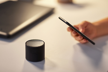 Image showing hand with smartphone and smart speaker at office