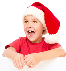 Image showing Little girl in santa hat is holding blank board