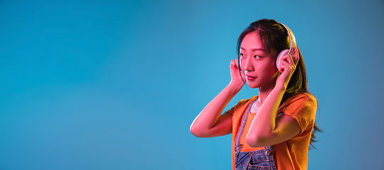 Image showing Asian young woman\'s portrait on blue studio background in neon. Concept of human emotions, facial expression, youth, sales, ad.
