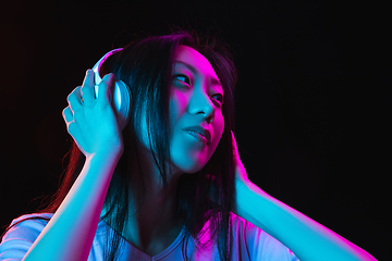 Image showing Asian young woman\'s portrait on dark studio background in neon. Concept of human emotions, facial expression, youth, sales, ad.