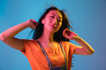 Image showing Asian young woman\'s portrait on blue studio background in neon. Concept of human emotions, facial expression, youth, sales, ad.