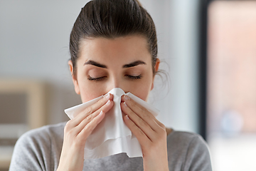 Image showing sick woman blowing nose in paper tissue at home