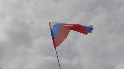 Image showing Russian flag on the flagpole waving in the wind against a blue sky with clouds. Slow motion