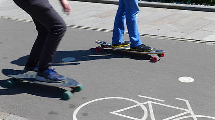 Image showing Feet of two boys riding on a skateboard ride on asphalt.