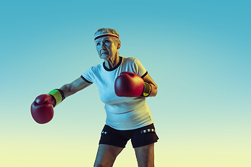 Image showing Senior woman boxing in sportwear on gradient background in neon light