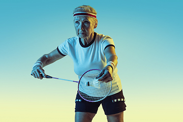 Image showing Senior woman playing badminton in sportwear on gradient background in neon light