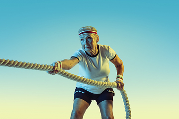 Image showing Senior woman training with ropes in sportwear on gradient background in neon light