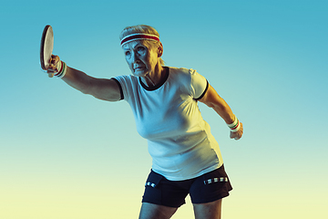 Image showing Senior woman training in table tennis in sportwear on gradient background in neon light