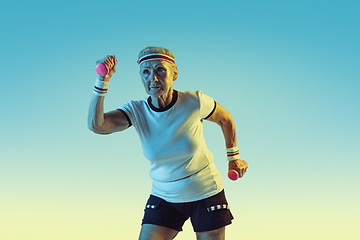 Image showing Senior woman training with weights in sportwear on gradient background in neon light