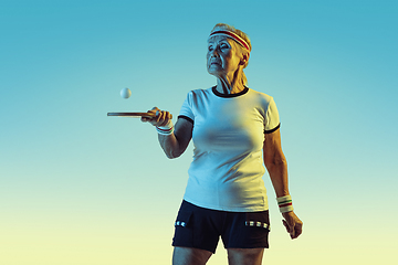 Image showing Senior woman training in table tennis in sportwear on gradient background in neon light