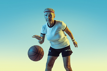 Image showing Senior woman playing basketball in sportwear on gradient background in neon light