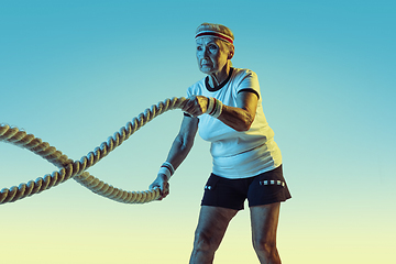 Image showing Senior woman training with ropes in sportwear on gradient background in neon light