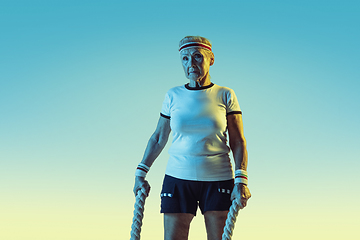 Image showing Senior woman training with ropes in sportwear on gradient background in neon light