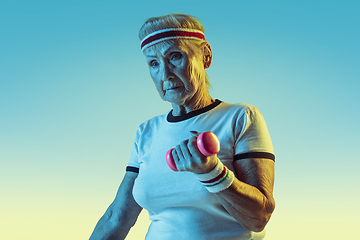 Image showing Senior woman training with weights in sportwear on gradient background in neon light