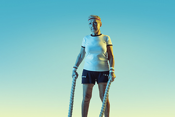 Image showing Senior woman training with ropes in sportwear on gradient background in neon light