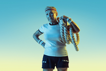 Image showing Senior woman training with ropes in sportwear on gradient background in neon light