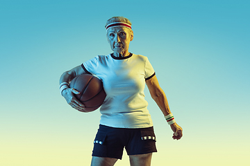 Image showing Senior woman playing basketball in sportwear on gradient background in neon light