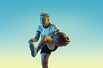 Image showing Senior woman playing basketball in sportwear on gradient background in neon light