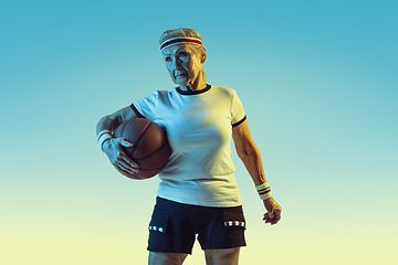 Image showing Senior woman playing basketball in sportwear on gradient background in neon light