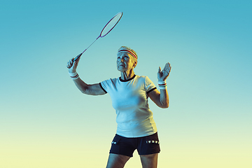 Image showing Senior woman playing badminton in sportwear on gradient background in neon light