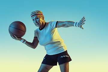 Image showing Senior woman playing basketball in sportwear on gradient background in neon light