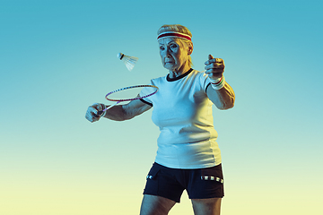 Image showing Senior woman playing badminton in sportwear on gradient background in neon light