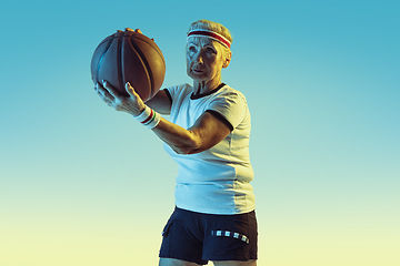 Image showing Senior woman playing basketball in sportwear on gradient background in neon light