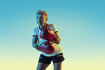 Image showing Senior woman boxing in sportwear on gradient background in neon light