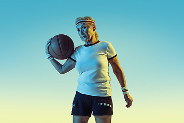 Image showing Senior woman playing basketball in sportwear on gradient background in neon light