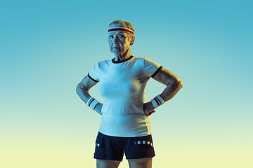 Image showing Senior woman training and posing in sportwear on gradient background in neon light