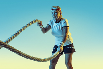 Image showing Senior woman training with ropes in sportwear on gradient background in neon light