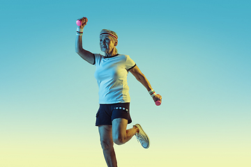 Image showing Senior woman training with weights in sportwear on gradient background in neon light