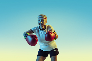 Image showing Senior woman boxing in sportwear on gradient background in neon light